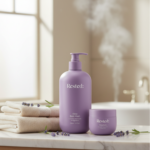 Purple 'Rested' body wash and cream on a bathroom counter with towels and lavender flowers.